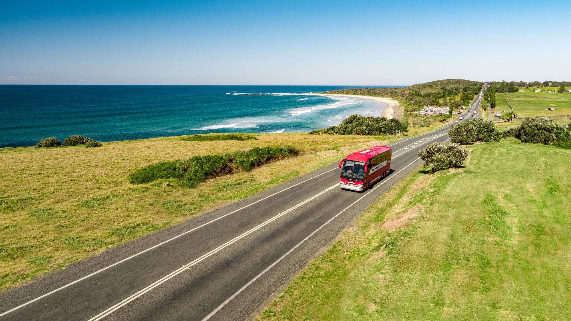 Greyhound coach on a coastal road above a turquoise bay backed by a mountain