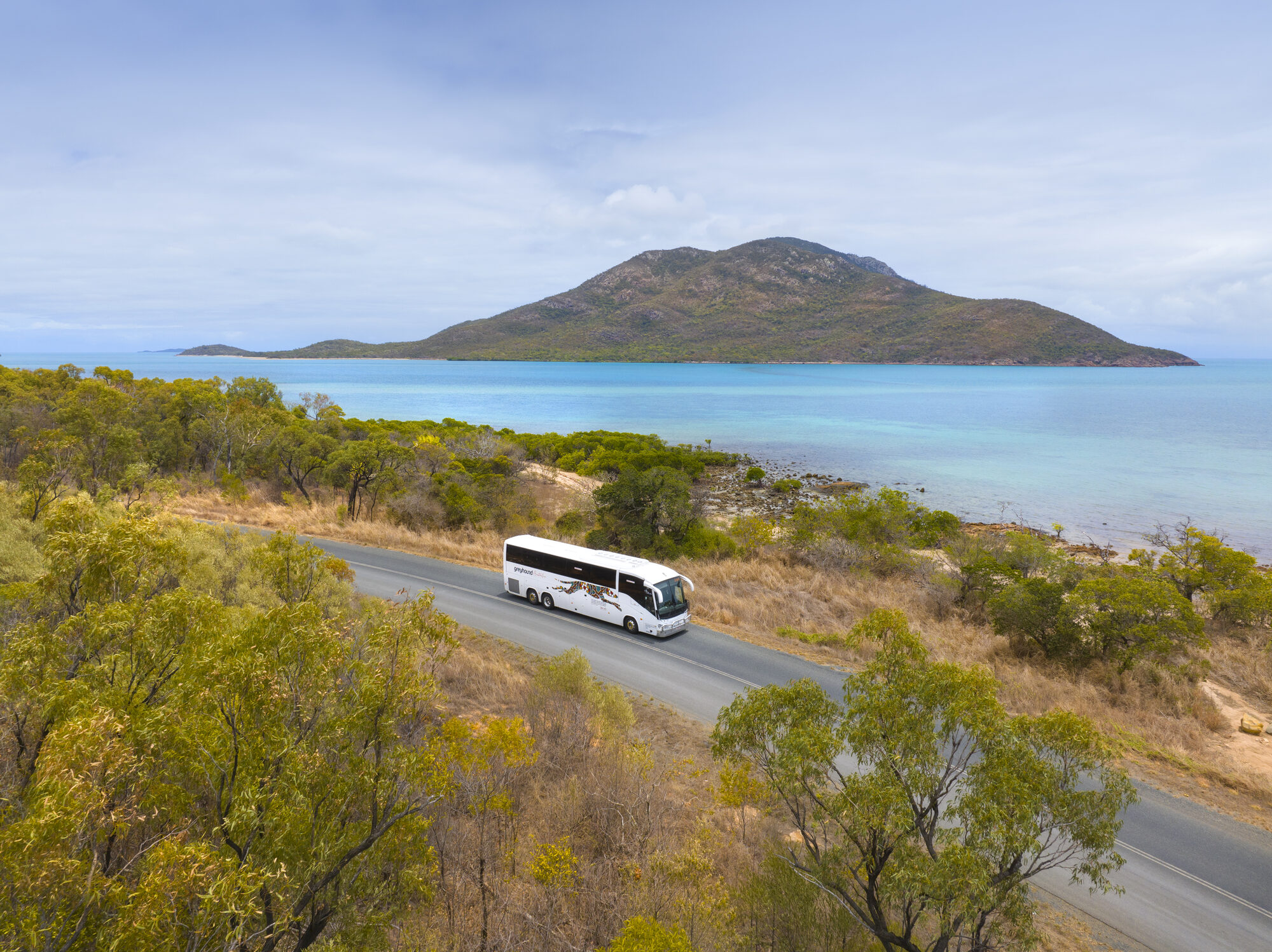 A red Greyhound Australia coach cruising a coastal highway above the ocean on the East Coast