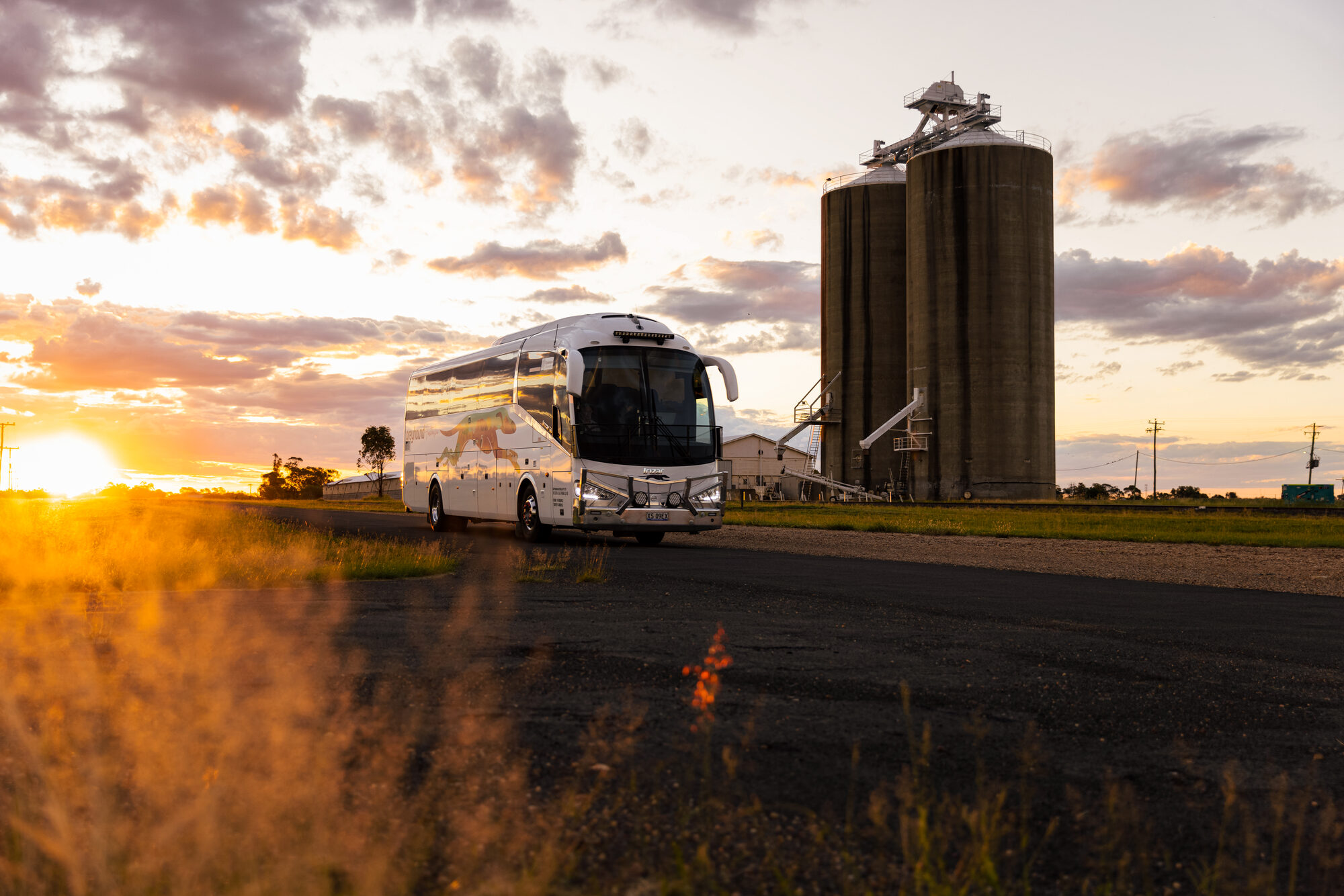 Greyhound coach at sunset beside grain silos in the Australian Outback