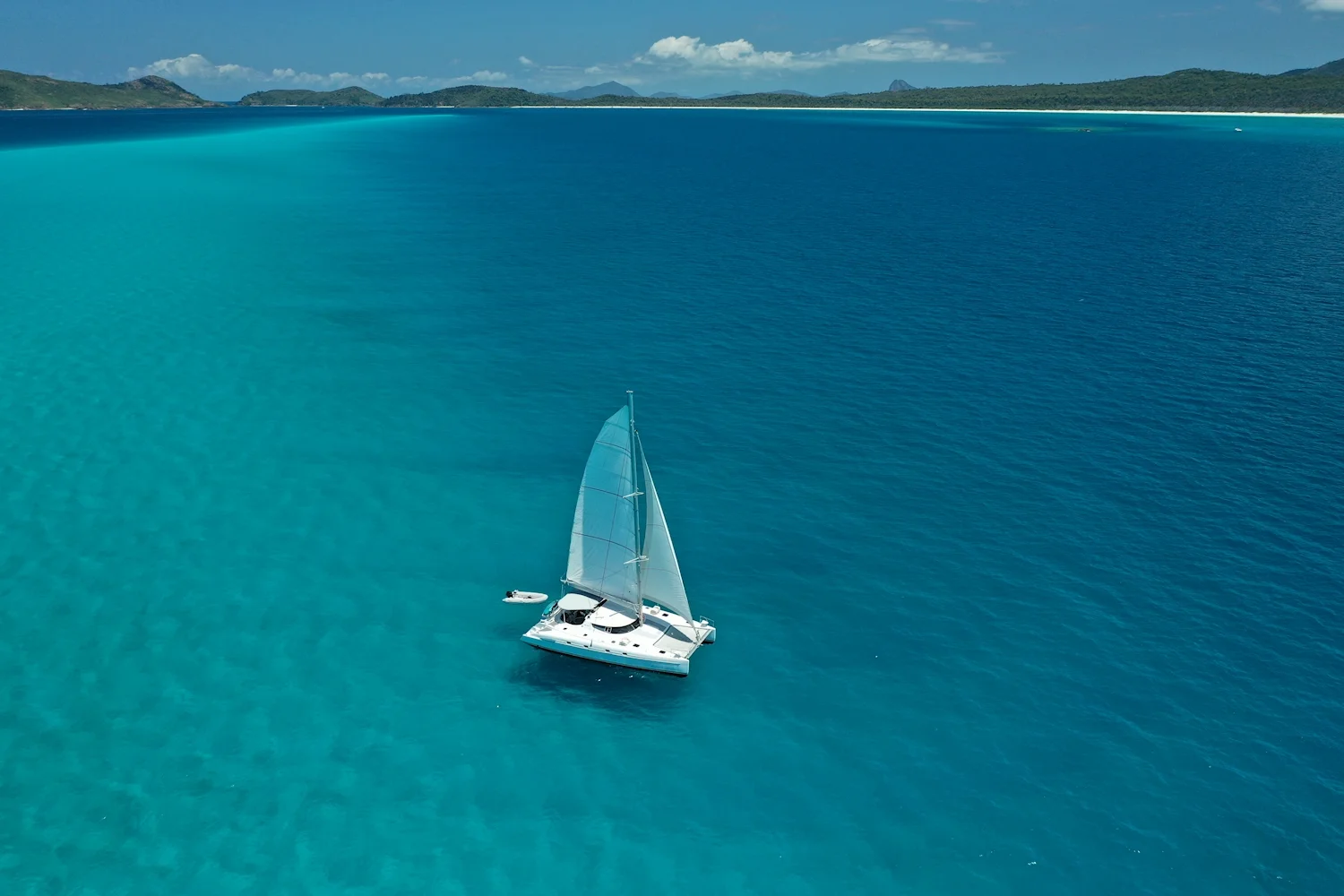 Sailing Catamaran Entice anchored in clear turquoise tropical waters under blue sky