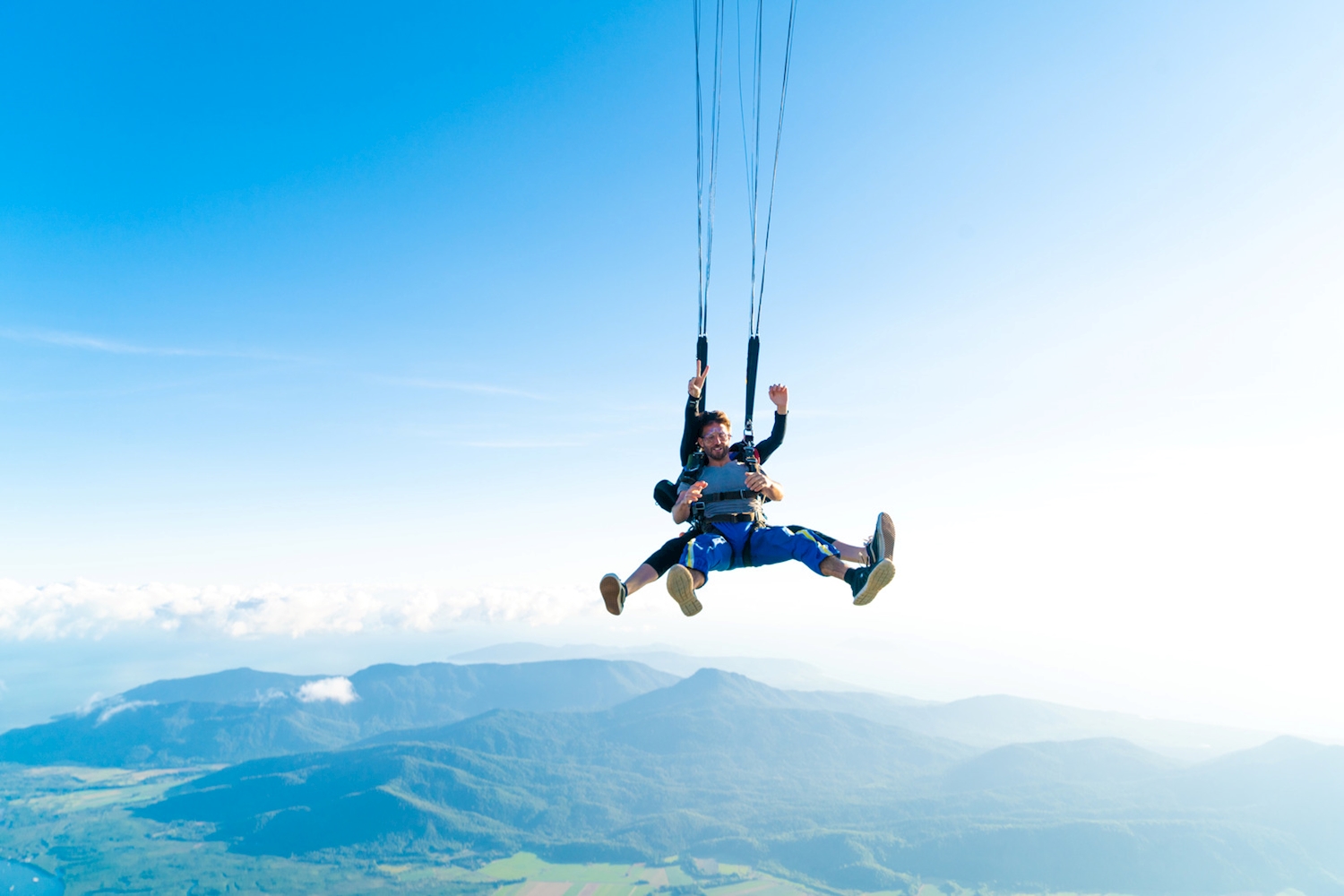 Tandem skydivers descending by parachute above Cairns rainforest and mountain ranges