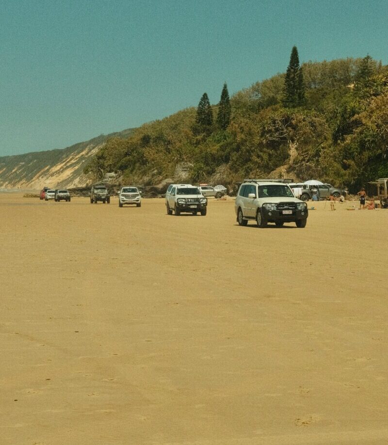 4WD tag-along tour convoy driving on 75 Mile Beach on K’gari (Fraser Island) with blue sky and ocean backdrop.