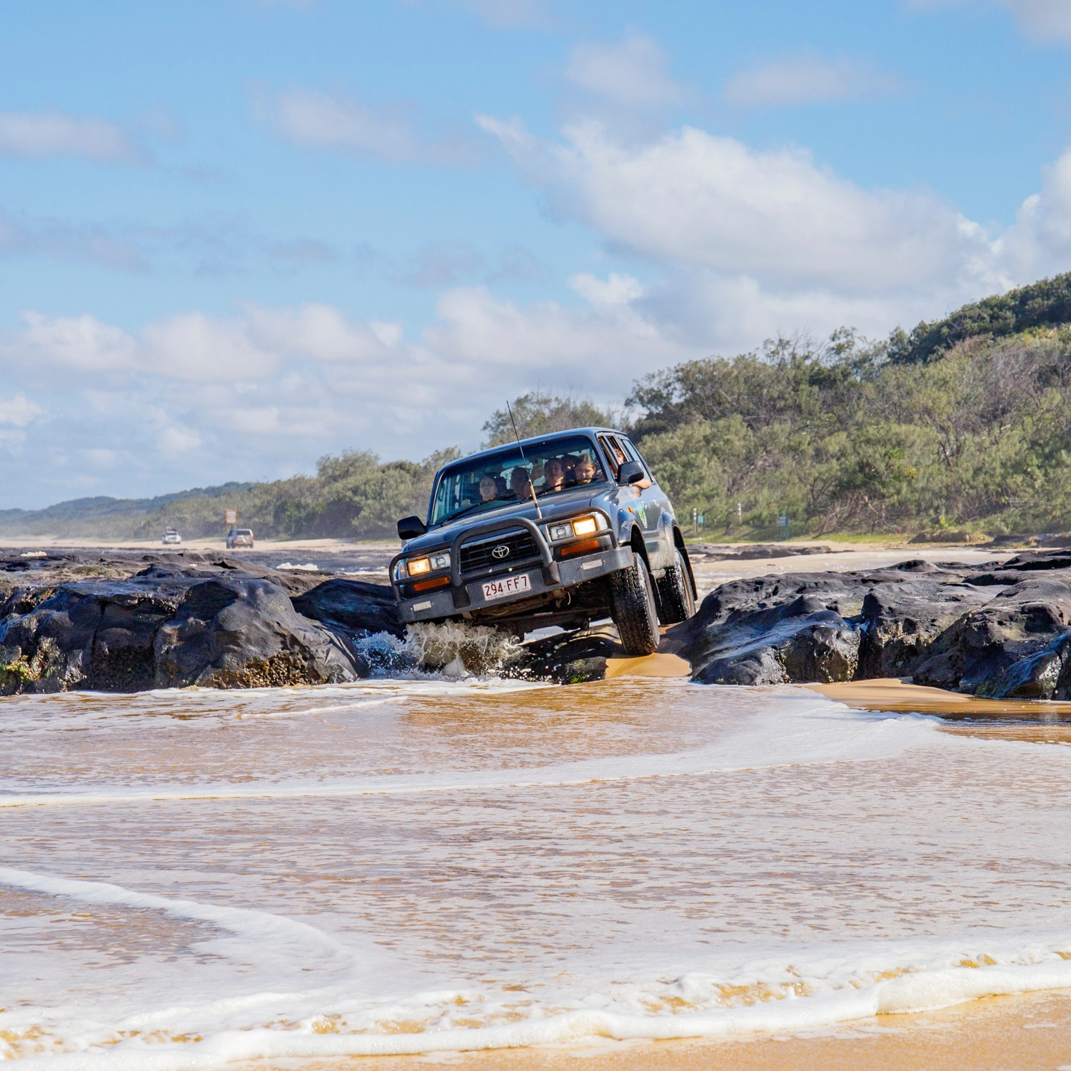 4WD vehicle crossing rocky beach section on K’gari Fraser Island
