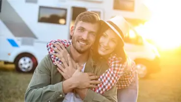 Couple hugging beside a campervan at a campsite during sunset