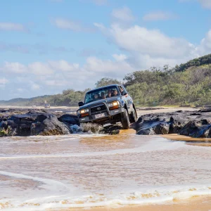 4WD vehicle crossing rocky beach section on K’gari Fraser Island