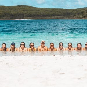 Group of travellers sitting in shallow clear water at Fraser Island lake