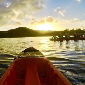 Dundee Adventure Travel | Go Sea Kayak | Byron Bay Sea Kayak Tour Sunrise Kayakers paddling in Byron Bay at sunrise with Cape Byron Lighthouse on the headland