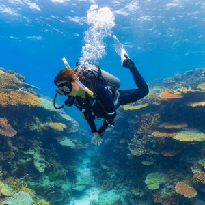 Female diver swimming over brightly coloured coral.