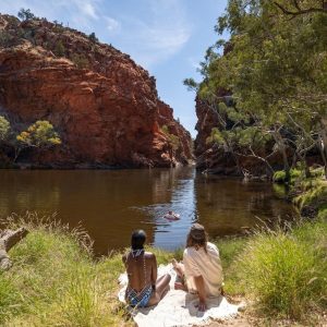 People relaxing by a river in a red rock gorge in the Australian Outback