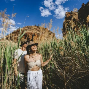 Couple walking through tall reeds in a rocky gorge in Central Australia