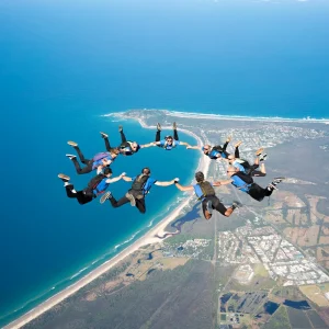 Group of skydivers holding formation above Byron Bay ocean and land