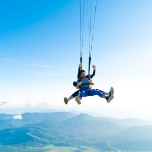 Tandem skydivers descending by parachute above Cairns rainforest and mountain ranges