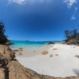 Sailing Catamaran Entice anchored off tropical island with white sand beach